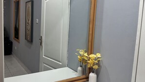 Un couloir avec une porte blanche, un miroir à cadre en bois et deux vases blancs ornés de fleurs jaunes.