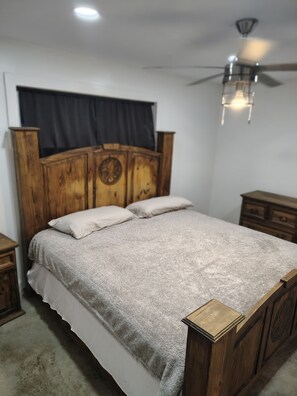 Een slaapkamer met een houten bed, wit beddengoed, een plafondventilator en een donker gordijn.