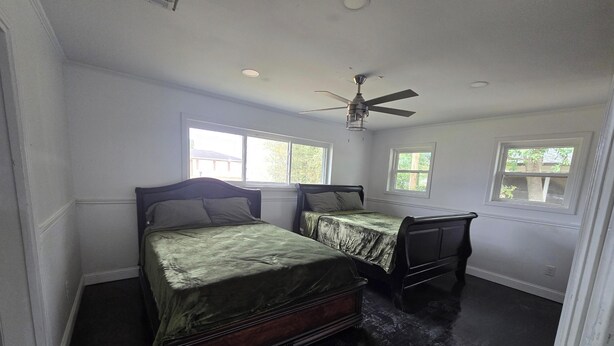 A bedroom with two beds, a ceiling fan, and windows with views of trees and a building. - Peaceful 3-bedroom house with AC in charming Jennings (Jennings)