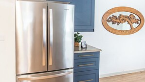 A kitchen with a stainless steel refrigerator, blue cabinets, a wooden floor, and a decorative wooden wall piece. - 4BR I Gameroom, Queen x4, Kitchens x2, Pac n' play (Fargo)
