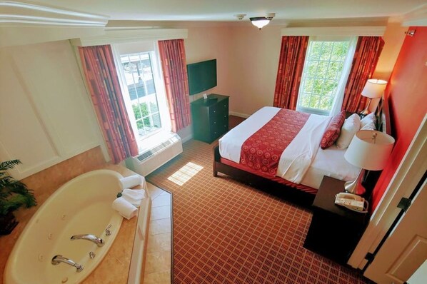 Une chambre d’hôtel avec un grand lit, une télévision, une salle de bain avec baignoire et une fenêtre avec des rideaux.