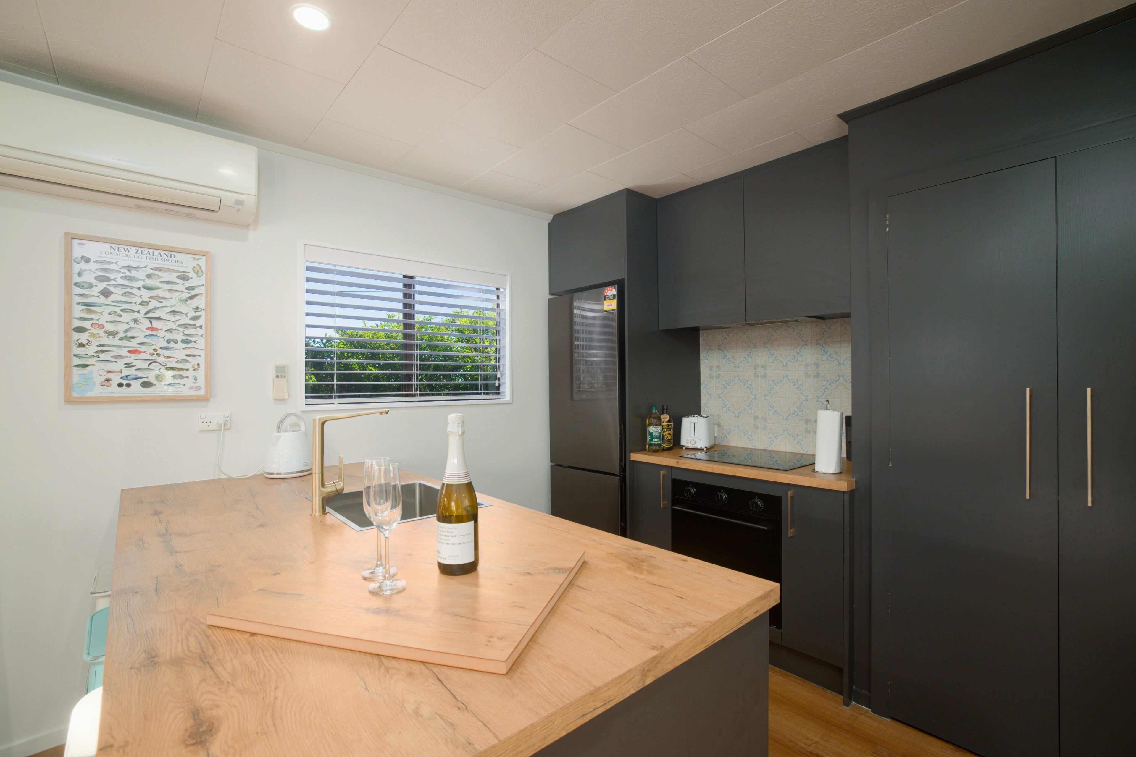 A modern kitchen with dark cabinets, a wooden countertop, a wine bottle, and a wine glass.