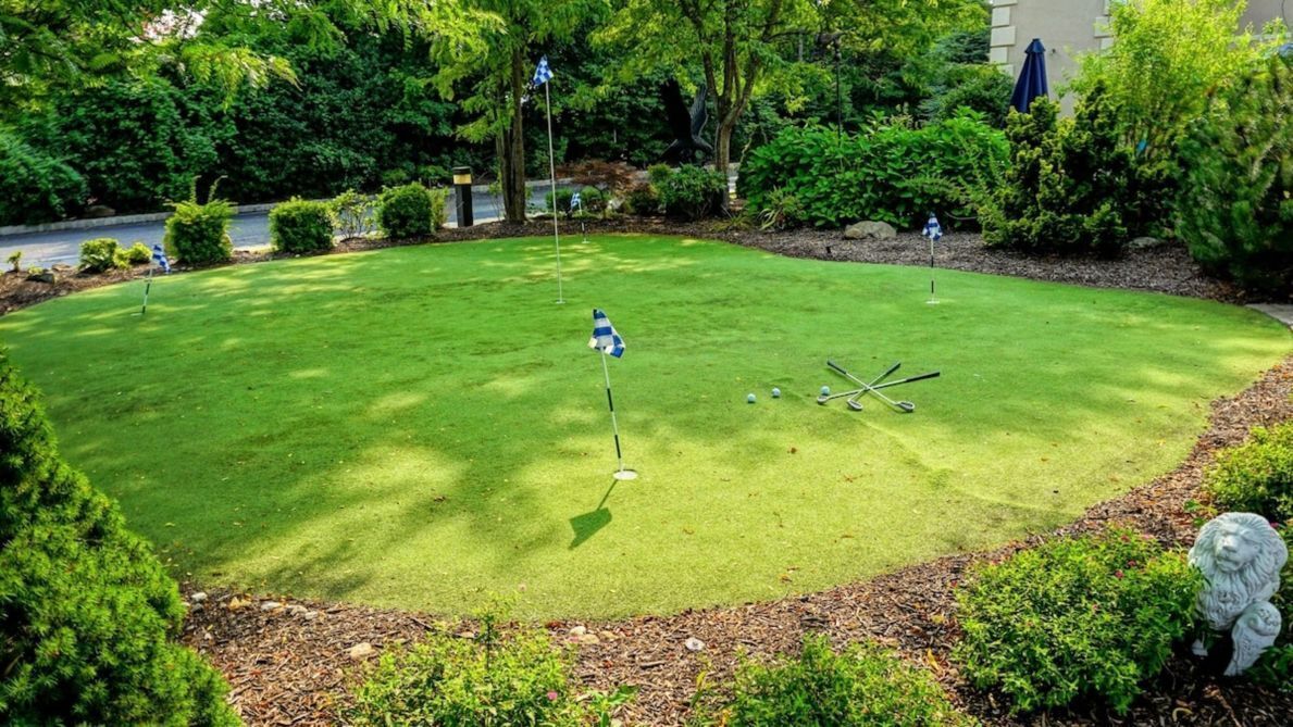 Ein gepflegter Golfplatz mit Putting-Green, umgeben von üppiger Vegetation und einer Statue.