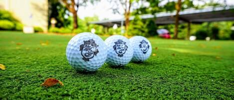 Trois balles de golf sur une surface verte, avec un arrière-plan flou composé d’arbres et d’un bâtiment.