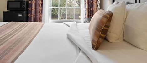 Una habitación de hotel con cama, mesita de noche, lámpara y ventana con cortinas.