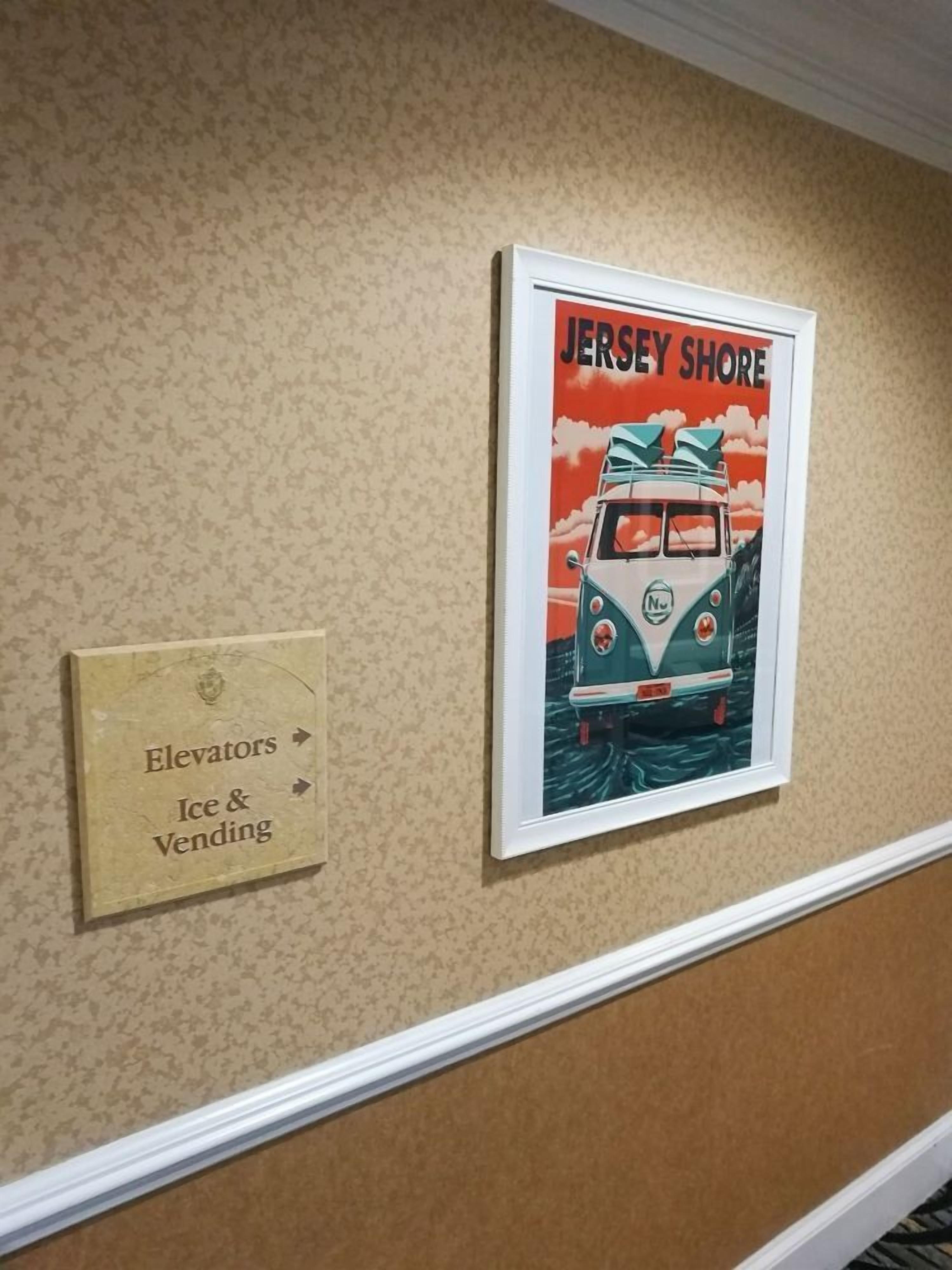 Un mur orné d’une affiche ancienne représentant une voiture, ainsi que d’un panneau indiquant l’emplacement des ascenseurs et d’un distributeur automatique de boissons et de produits divers.