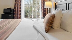 Ein Hotelzimmer mit Bett, Nachttisch, Lampe und einem Fenster mit Vorhängen.