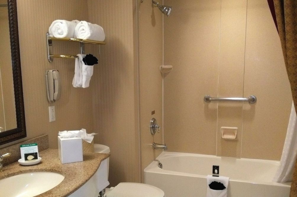 A bathroom with a sink, toilet, and bathtub. There are towels on a rack, a mirror, and a telephone.