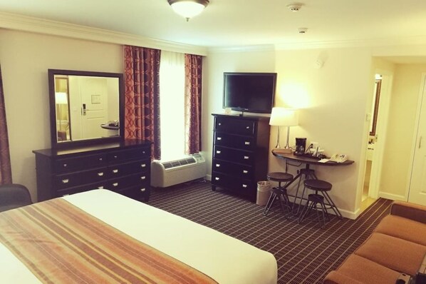 Ein Hotelzimmer mit einem großen Bett, einem Fernseher, einem Schreibtisch mit Lampe und einem Spiegel.