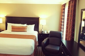 Ein Hotelzimmer mit einem großen Bett, zwei Nachttischen, einem Sessel und einem Spiegel.