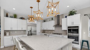 Une cuisine moderne avec des meubles blancs, un grand îlot central, des appareils en acier inoxydable et des luminaires suspendus originaux en forme d’étoile.
