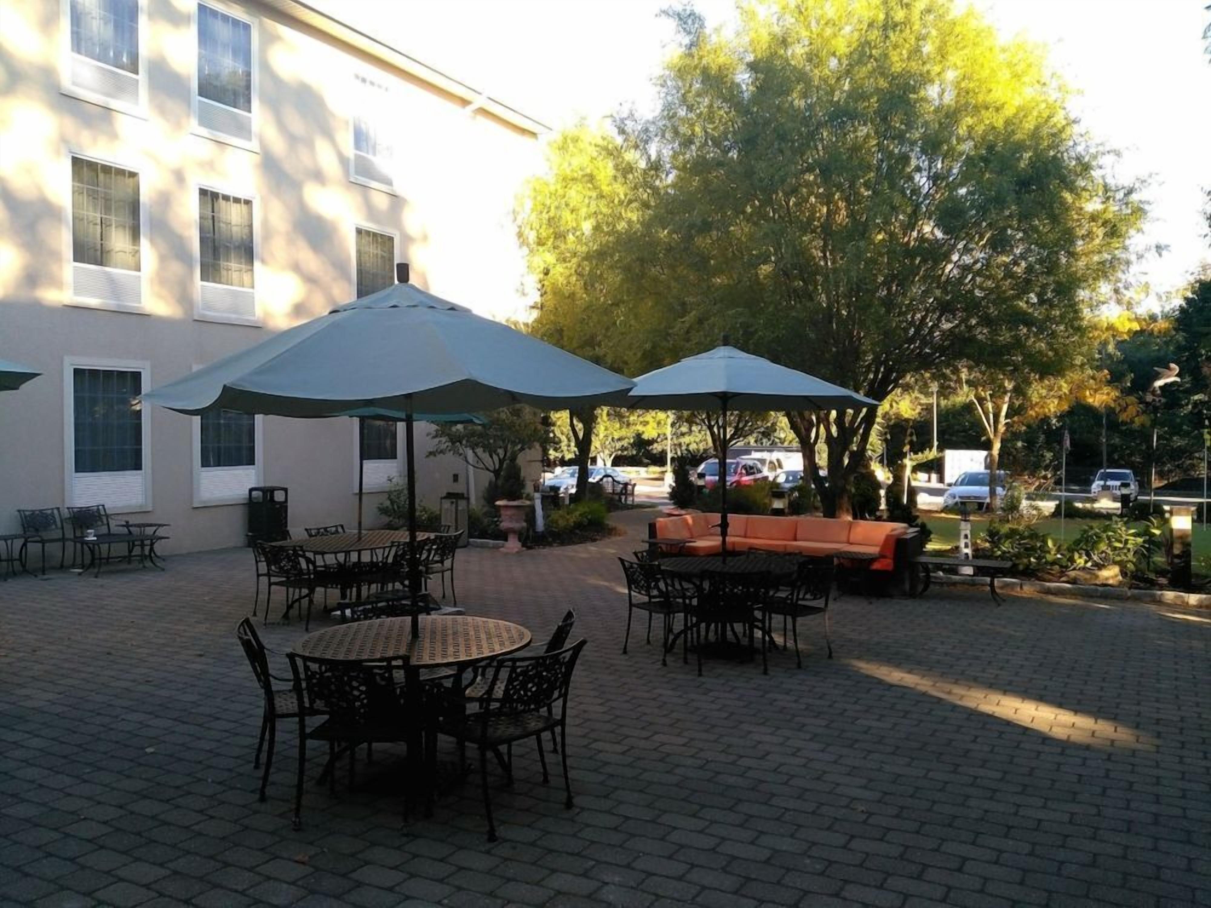 Un patio al aire libre con mesas, sillas, sombrillas y un área de estar.
