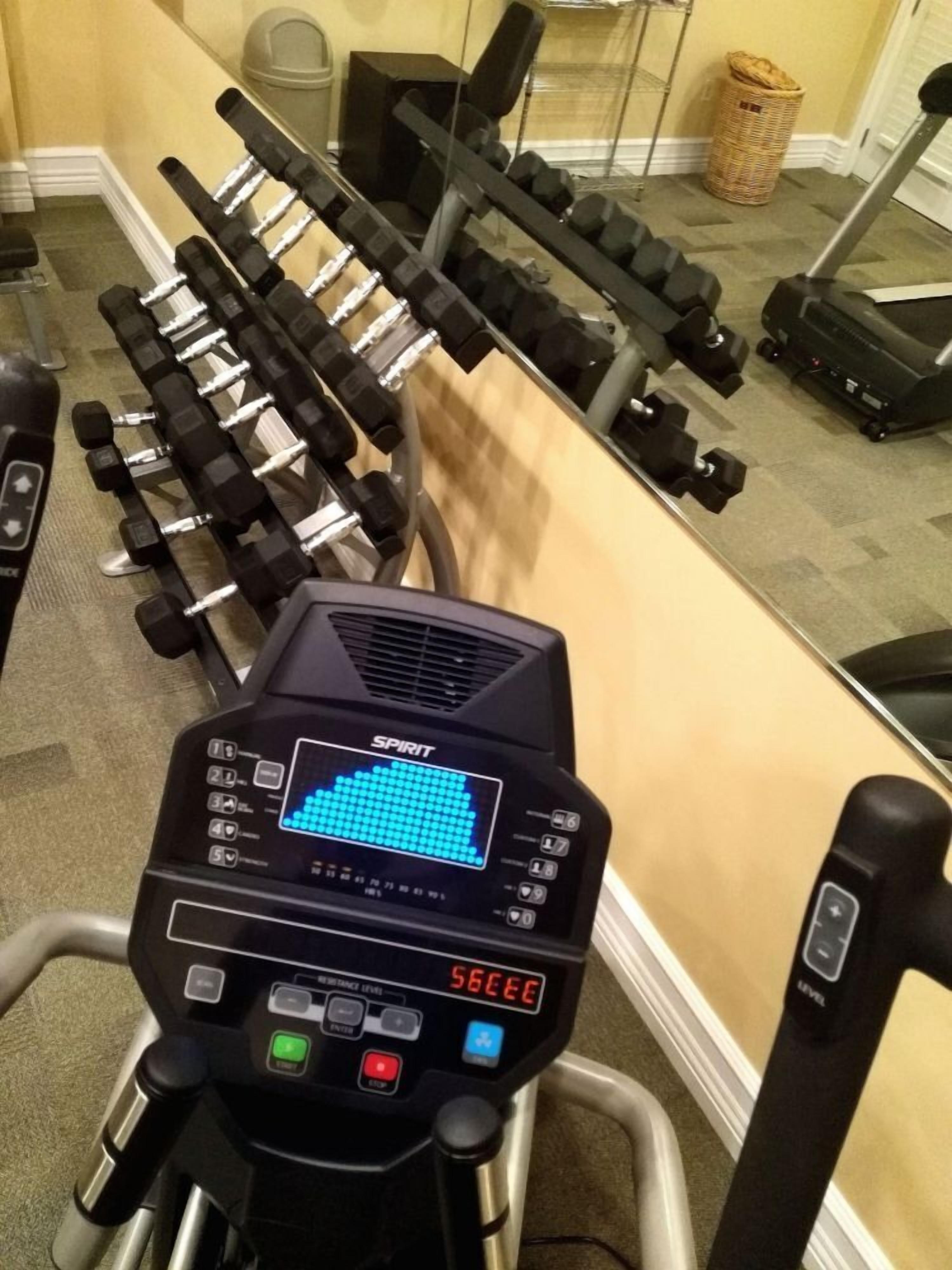 Un gimnasio con cinta de correr, mancuernas y una pantalla digital.