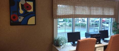 Una habitación con un escritorio, dos monitores y dos sillas. Hay una ventana que da a un estacionamiento y un edificio.