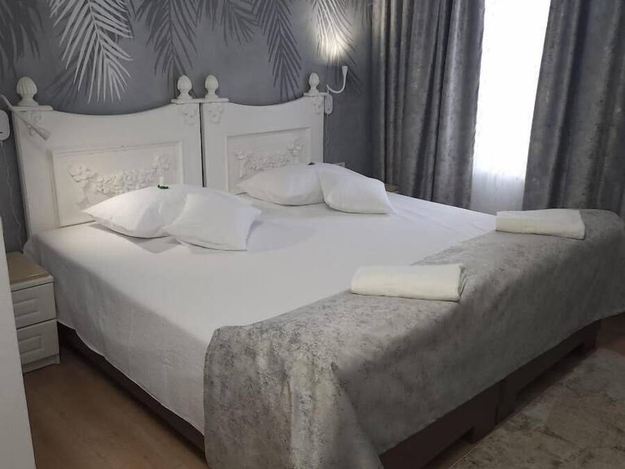 A neatly made bed with white linens and pillows, a wooden headboard with decorative carvings, and a grey patterned wall behind it.