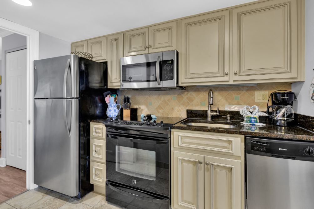 A modern kitchen with stainless steel appliances, beige cabinetry, and a granite countertop.