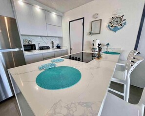 Une cuisine moderne avec des meubles blancs, une cuisinière noire et un îlot central blanc agrémenté de sets de table bleus.