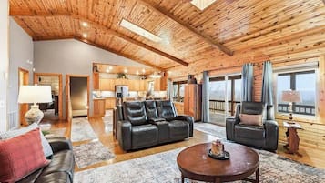 A spacious living area with a high wooden ceiling, a leather sofa, a coffee table, and a view through large windows.