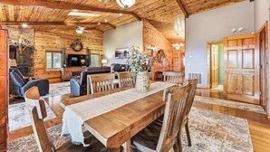 Een rustiek houten interieur met een eettafel, stoelen, een open haard en een zithoek met banken en een televisie.