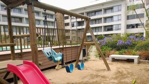 Un parque infantil con un tobogán rojo, columpios y una zona de juegos con arena.
