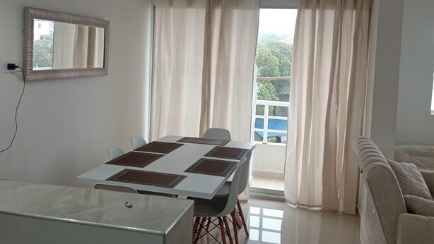 Una sala de estar moderna con comedor, sofá, un ventanal con cortinas y una lámpara en el techo.