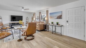 Una sala de estar moderna con un sofá, sillones, una mesa de centro, un televisor y un cuadro en la pared.