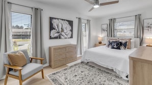 Un dormitorio con cama, mesita de noche, silla, cómoda y ventilador de techo.