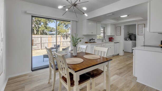 Una cocina moderna con armarios blancos, una mesa de comedor de madera y un amplio ventanal con vistas a un patio trasero.