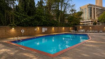 Piscina retangular com interior azul, rodeada por um muro de tijolos e árvores.
