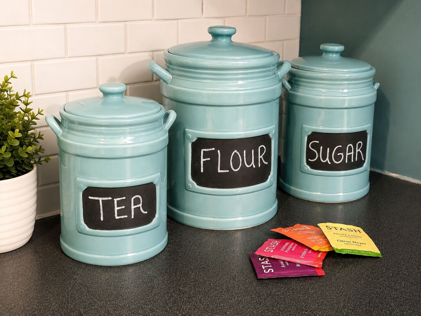 Three light blue kitchen storage containers with labels for tea, flour, and sugar.