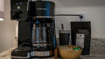 A Hamilton Beach coffee maker, a coffee cup, a bag of coffee, and a bowl on a kitchen counter.