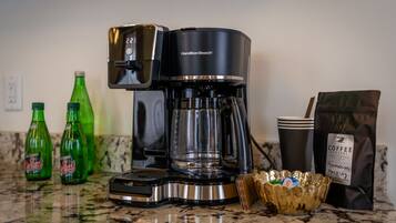 Una cafetera, botellas de refresco verde, una bolsa de café y un bol sobre una encimera de cocina.
