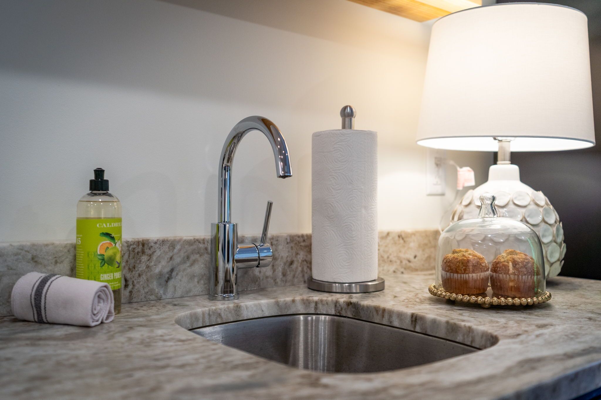 A bathroom sink with a modern faucet, a roll of toilet paper, a bottle of Caldera ginger mouthwash, and a lamp with a decorative glass dome.