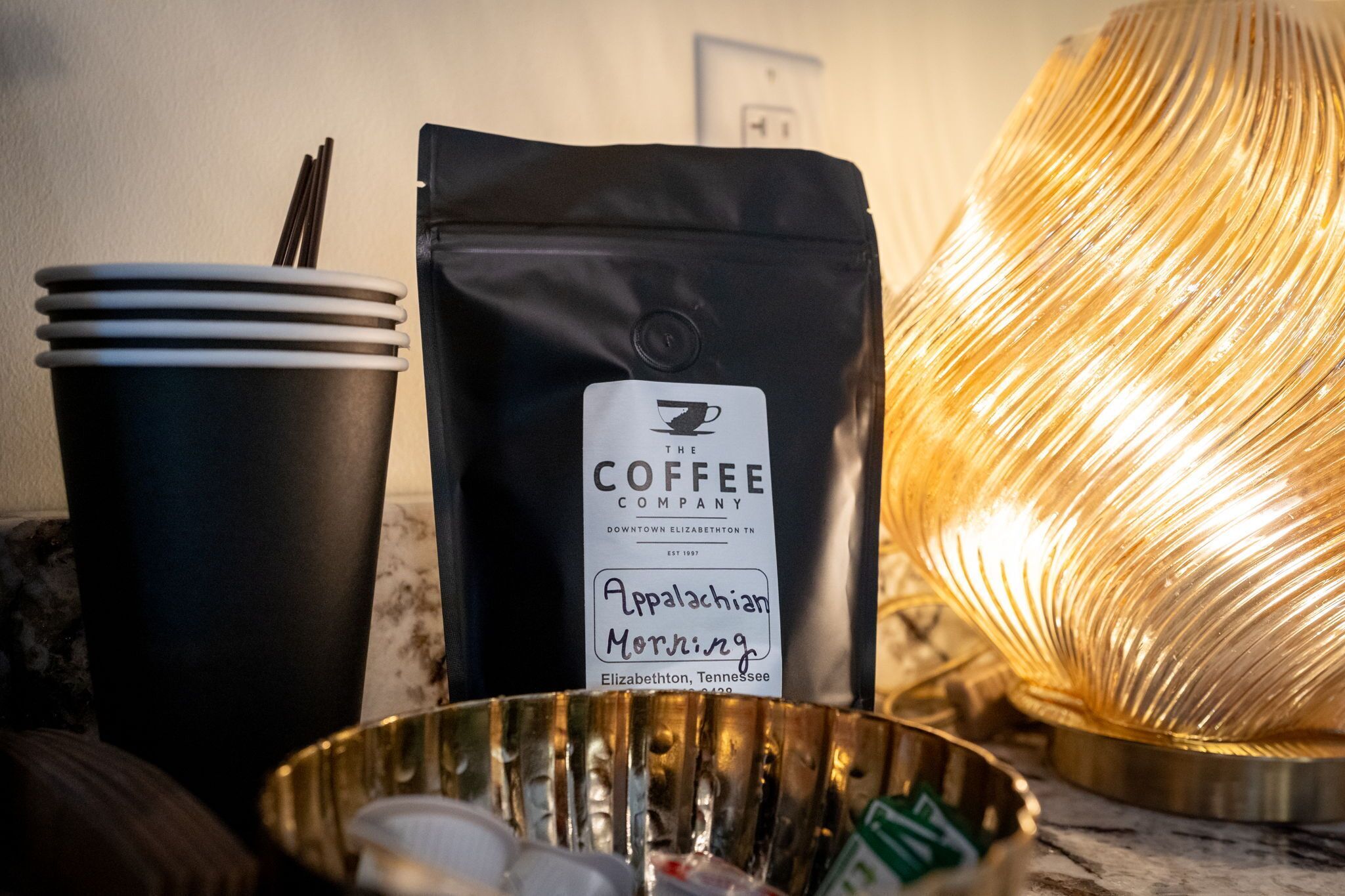 A coffee bag, disposable cups, and a metal bowl with utensils.