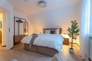 A modern bedroom with a large bed, bedside tables, a hanging light, and a potted plant. - Modern 75-square-meter apartment with a balcony - Quiet location near Winterberg (Winterberg)