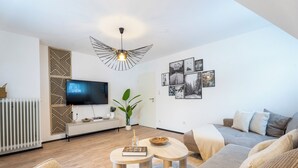 Ein modernes Wohnzimmer mit einem Flachbildfernseher, einer außergewöhnlichen Deckenleuchte und einer Wand, die mit gerahmten Fotos geschmückt ist.