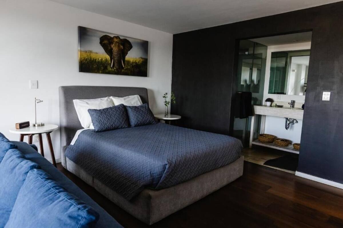 A bedroom with a bed, a bedside table, a nightstand, a mirror, and a wall-mounted picture.