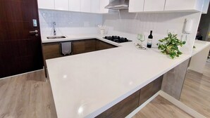 Une cuisine moderne avec des meubles blancs, un évier en acier inoxydable, une cuisinière à gaz et un plan de travail sur lequel se trouvent une bouteille de vin et des verres.