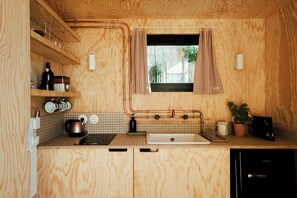 Eine kleine Küche mit Holzschränken, einem Fenster mit karierten Vorhängen, einer Spüle und einer Kaffeemaschine.