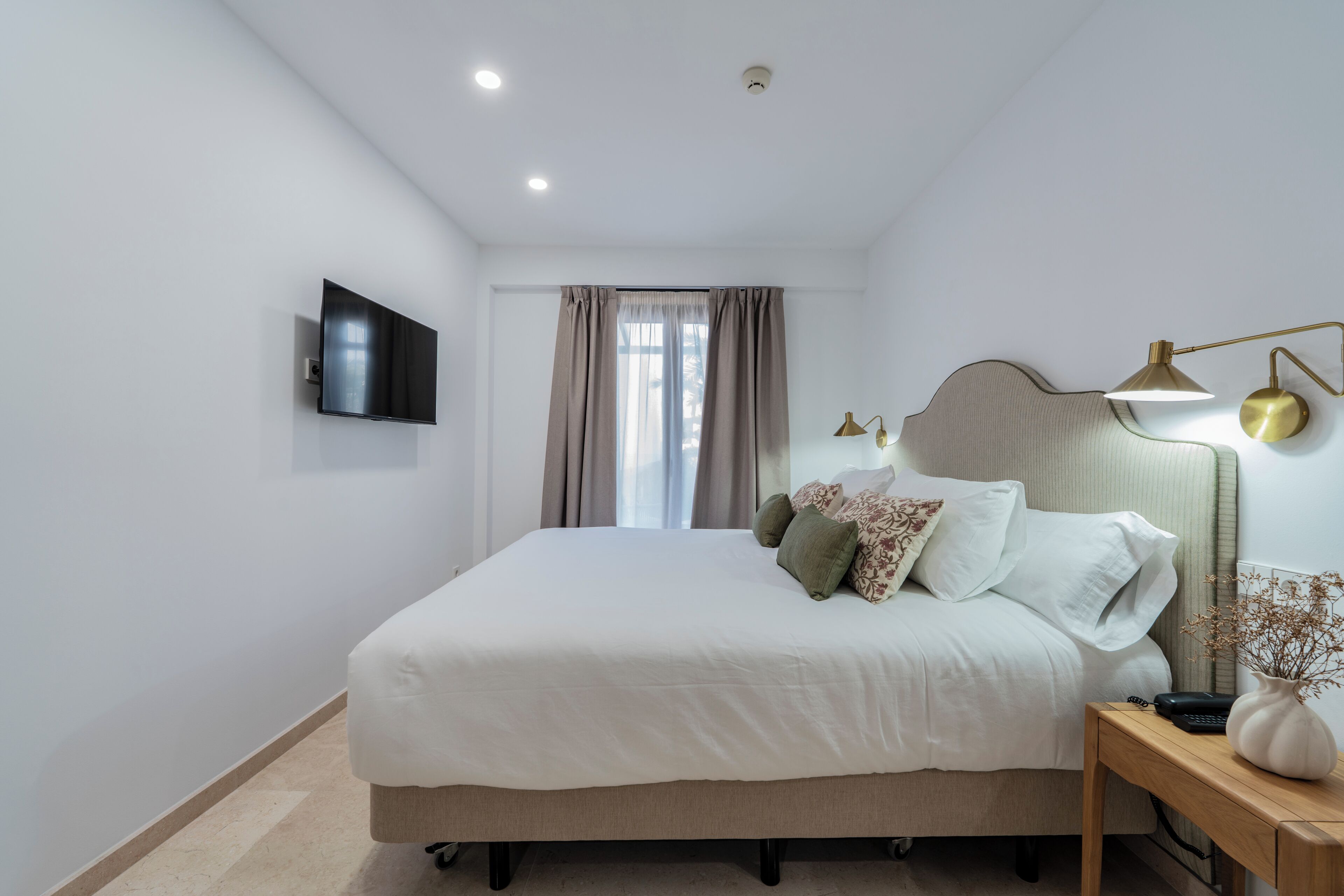 Une chambre à coucher avec un lit, une table de chevet, une lampe et un téléviseur fixé au mur.