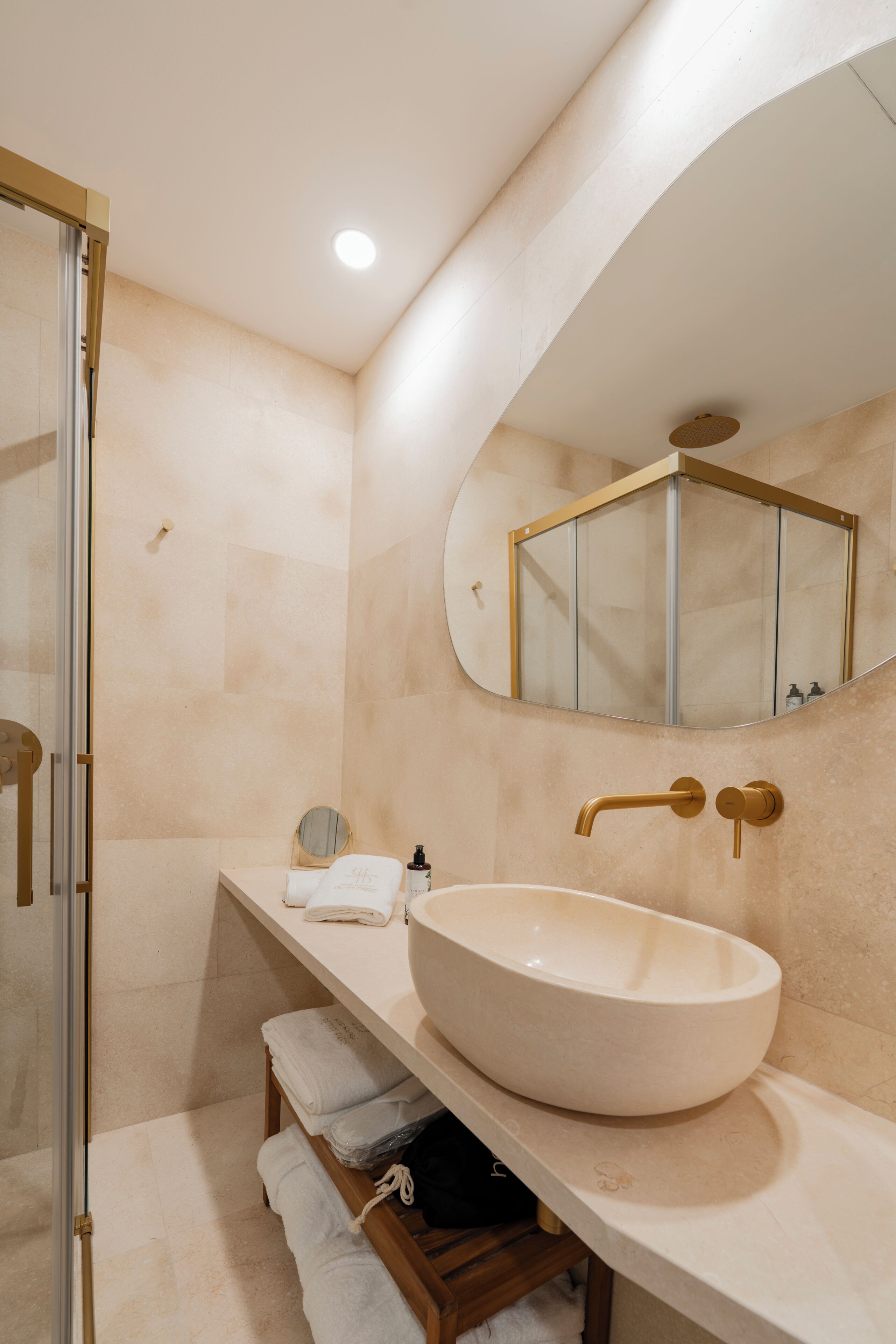 A modern bathroom with a large oval sink, a glass shower enclosure, and a mirror with a gold frame.