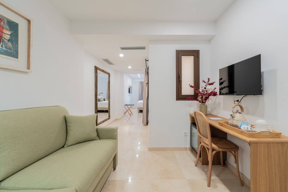 A room with a green sofa, a wooden desk, a chair, a flat-screen TV, and a mirror on the wall.