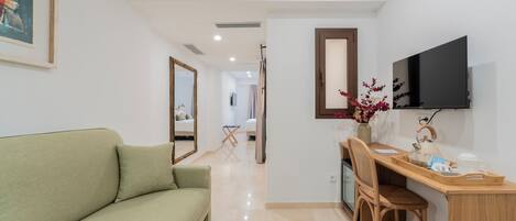 A room with a green sofa, a wooden desk, a chair, a flat-screen TV, and a mirror on the wall.