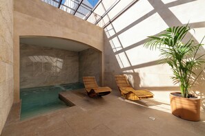 Un área de spa con piscina, tumbonas de madera y una planta en maceta.