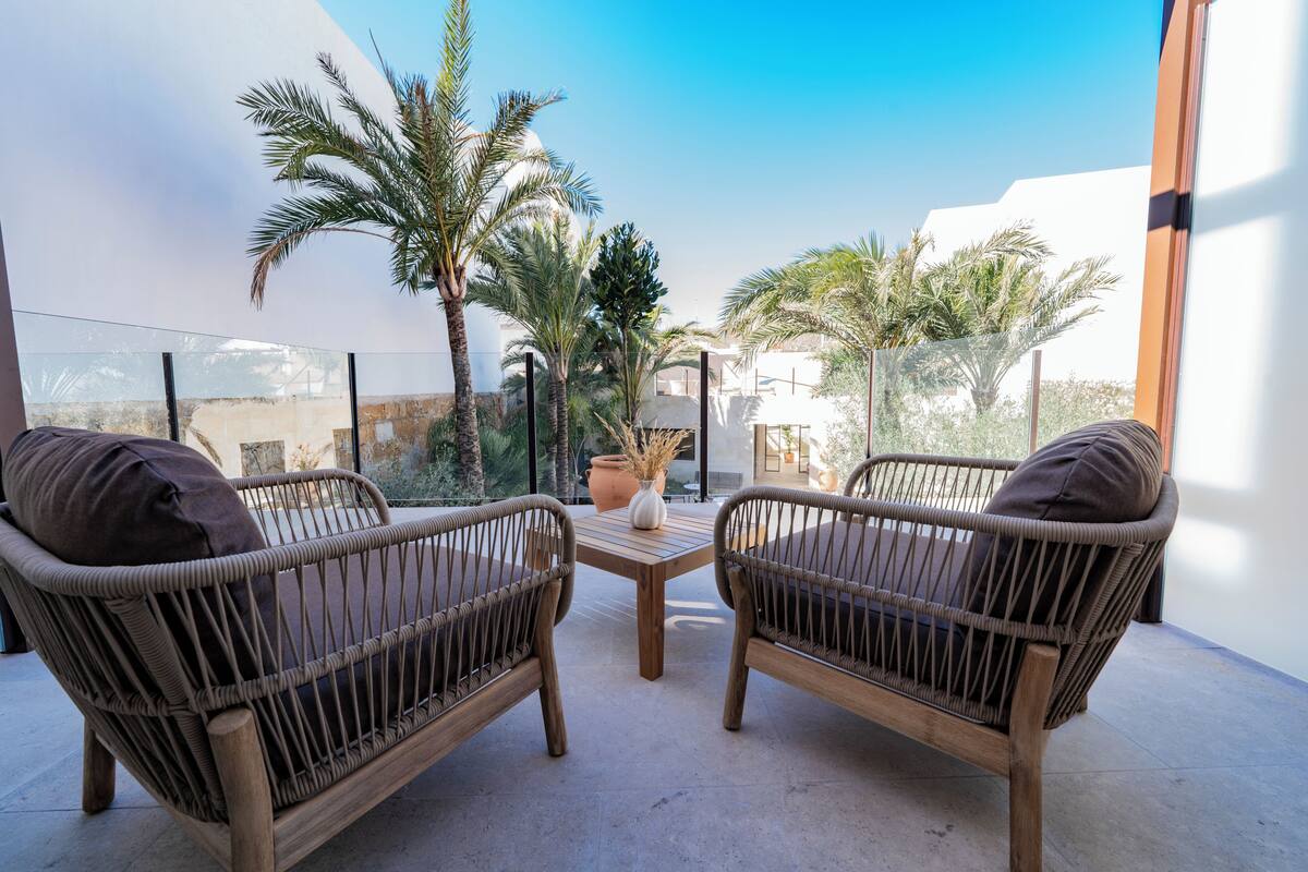 A balcony with wicker furniture, a potted plant, and a view of palm trees.
