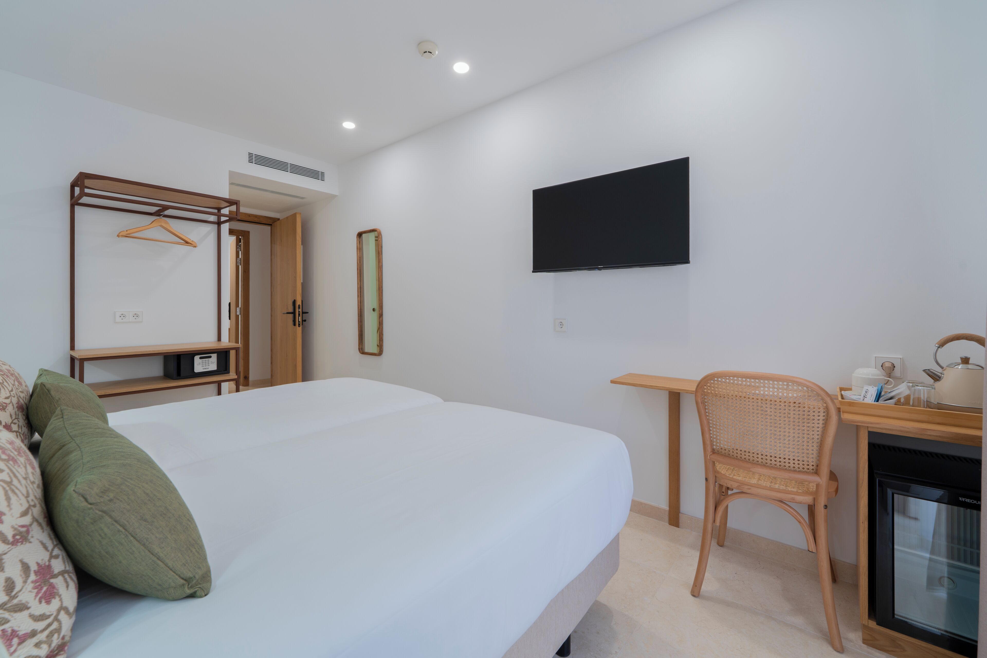 A hotel room with a bed, a desk with a chair, a television, and a small kitchenette.