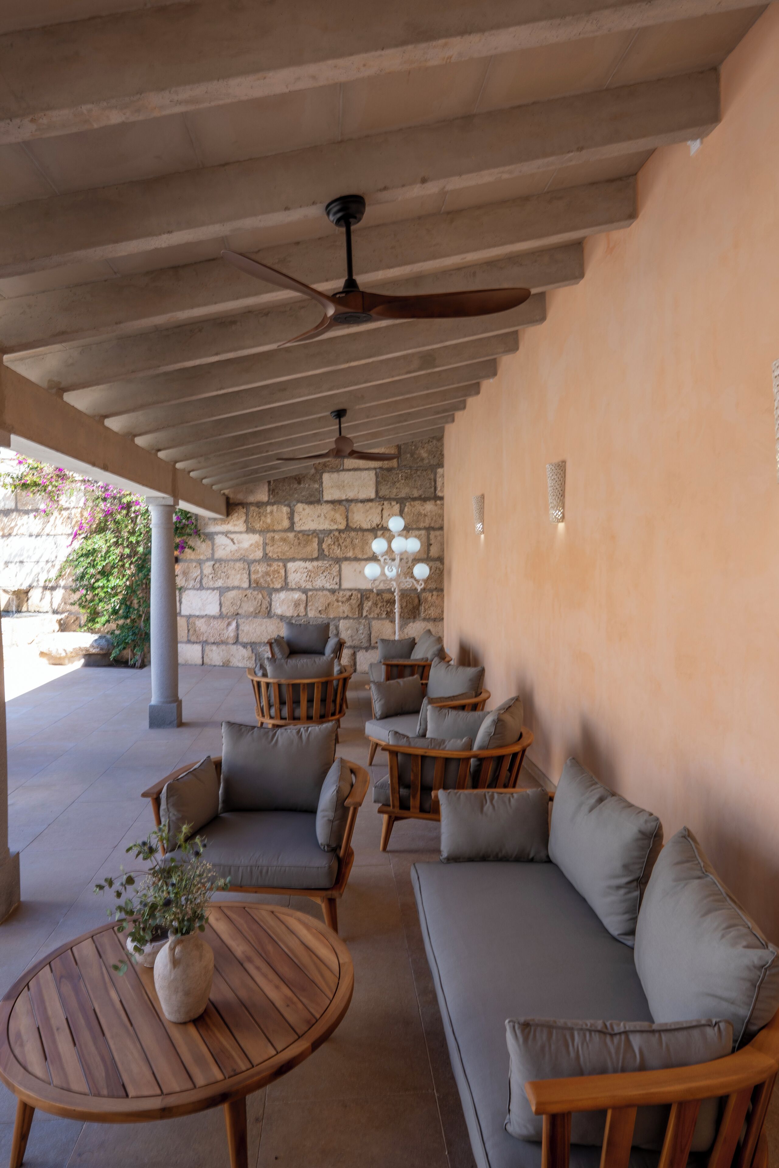An outdoor seating area with a stone wall, wooden furniture, and a ceiling fan.