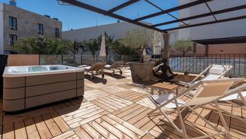 Terraza de madera con sillones, jacuzzi y plantas en macetas.