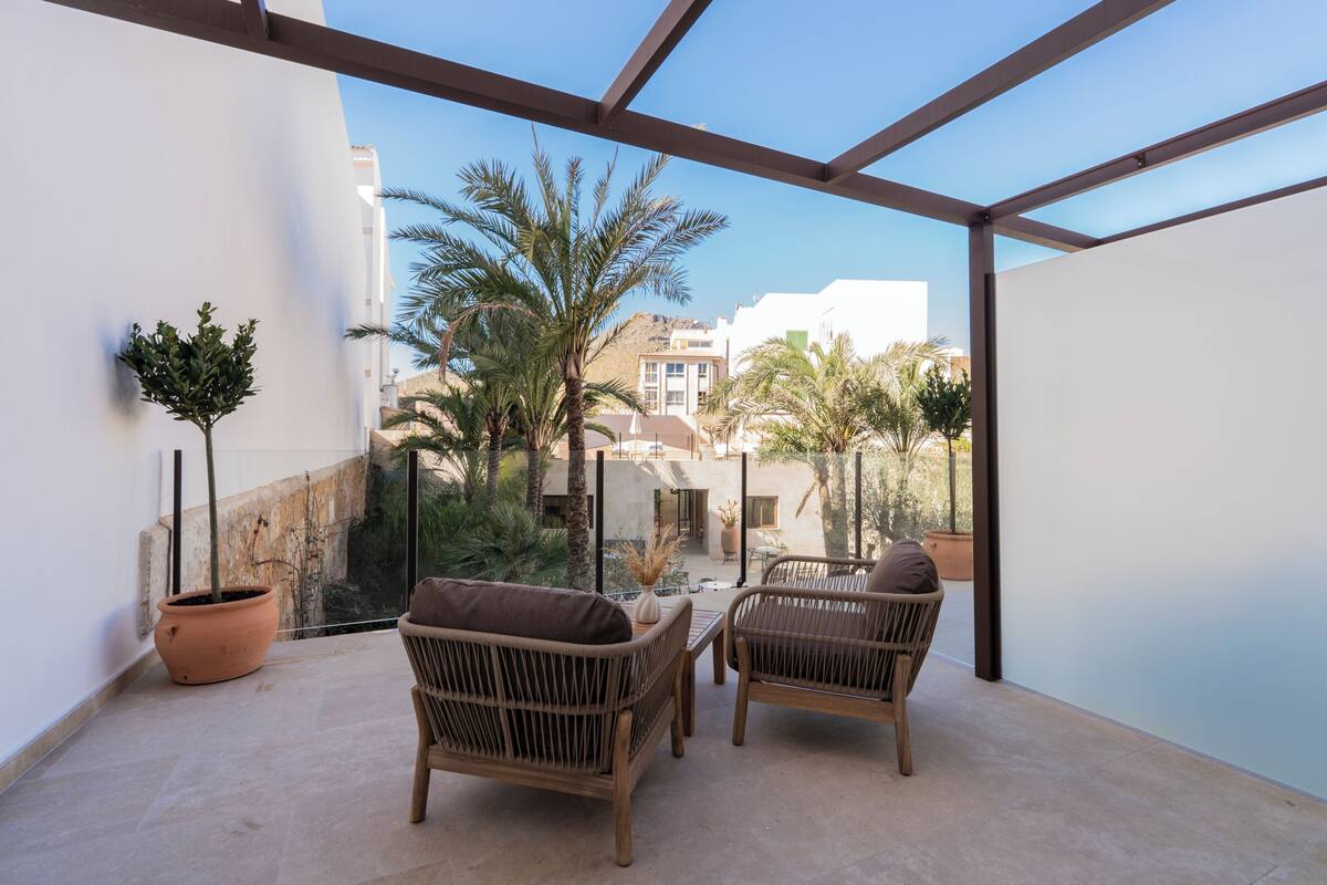 A balcony with wicker furniture, a potted plant, and a view of buildings and palm trees.