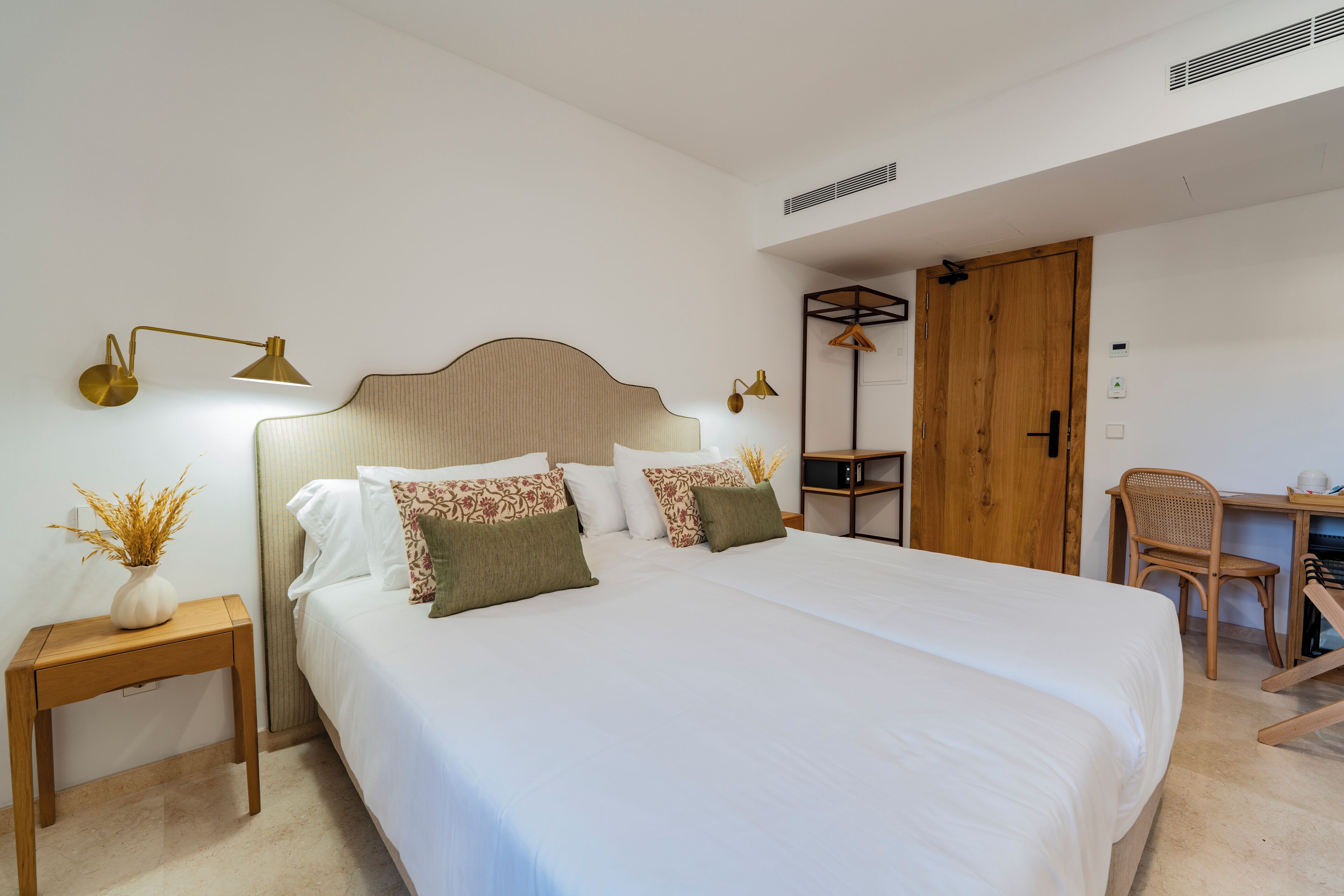 A neatly arranged bedroom with a bed, bedside table, lamp, and a desk with a chair.